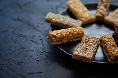 Different kind of granola fitness bars placed on black ceramic plate on a table. Healthy diet concept. Top view with copy space.の写真素材