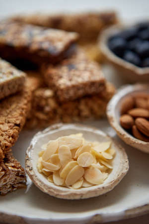 Close up of Almond petals. With various energy nutrition bars in background. Granola bars on ceramic plate over white background. With almonds, and berries on side. Healthy breakfast.の写真素材