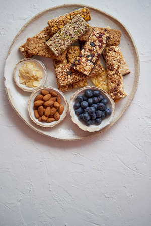 Mixed composition of energy nutrition bar, granola on ceramic plate over white background with copy space. Healthy breakfast. Top view, flat layの写真素材