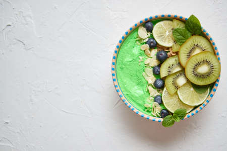 Green smoothie or yogurt bowl. With fresh kiwi, blueberries, lime and almond flakes. Healthy breakfast concept. Top view, flat lay. With copyspace.の写真素材