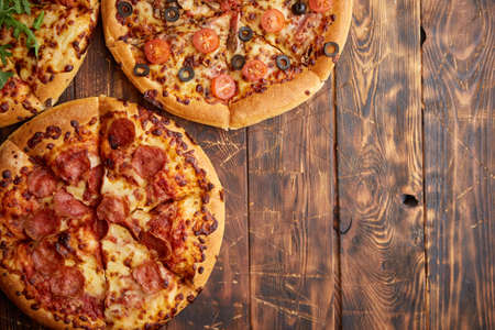 Composition of three various kinds pizzas placed on rusty scratched wooden table. Hot and fresh food ready to eatの写真素材