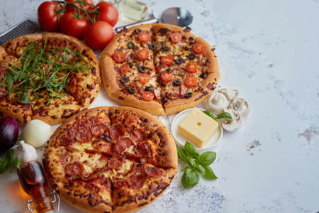 Three american style pizzas with thin fluffy dough served on a table. Placed with various ingredients on side.の写真素材