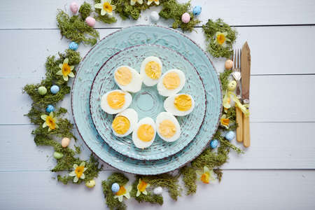 Easter table setting with flowers and eggs. Decorative ceramic plates with boiled eggs halfs. Rustical dishware. View from above.の写真素材