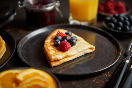 Tasety homemade pancake on black ceramic plate. Placed on dark rusty table. With fresh fruits,...