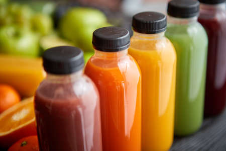 Colorful bottles filled with fresh fruit and vegetable juice or smoothie. Placed in row on black wooden table.の写真素材