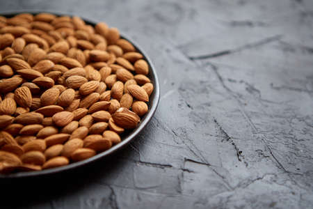 Whole almond nuts in black plate placed on black stone table. Healthy vegetarian snack. Copy space for text.の写真素材