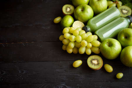 Mixed green fruits and vegetables placed on black wooden table. With botteled juice or smoothie. Healthy diet concept.の写真素材