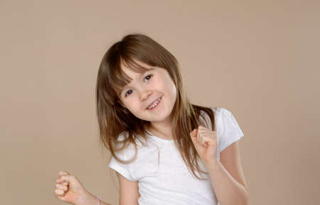 Cute little girl in white tshirt dancing, smiling and having fun in studio session. Posing over beige background. Isolated.の写真素材