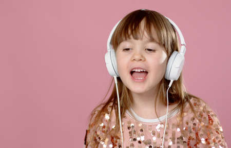 Pretty 6 or 7 years old little girl singing and dancing with headphones. While posing on pink...