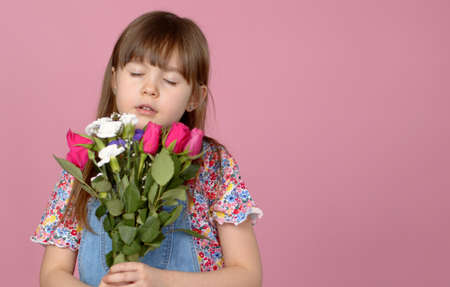 Cute smiling adorable child girl holding bouquet of spring flowers isolated on pink background in studio.の写真素材