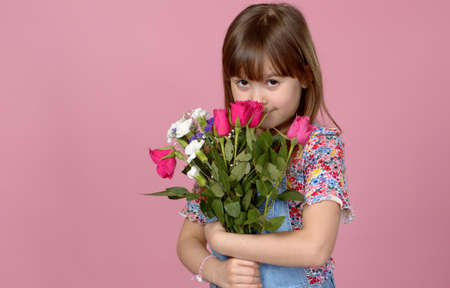 Sweet adorable young little girl holding bunch of fresh spring flowers. Wearing dungarees. Isolated...