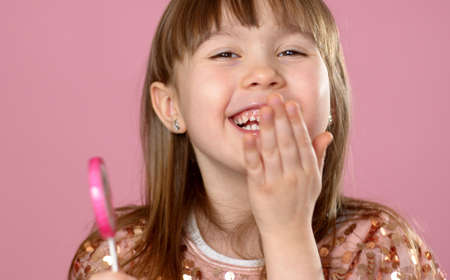 Adorable young girl posing with pink lollypop candy. Smiling to the camera with all happyness....
