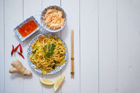 Tasty and Fresh Noodles with Chicken and vegetables served on ceramic plate with chopsticks, sauce, ginger, on side.の写真素材