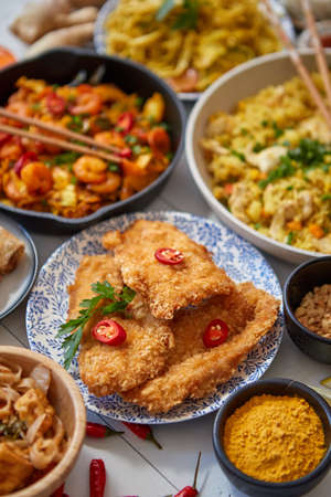 Asian food served. Plates, pans and bowls full of tasty oriental dishes. Noodles chicken stir fry and vegetables ingredients with spices, sauces and chopsticks on whie wooden background.の写真素材