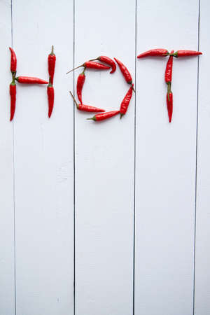 A word HOT formed with small red chilli peppers. Placed on white wooden table. Top View with copy spaceの写真素材
