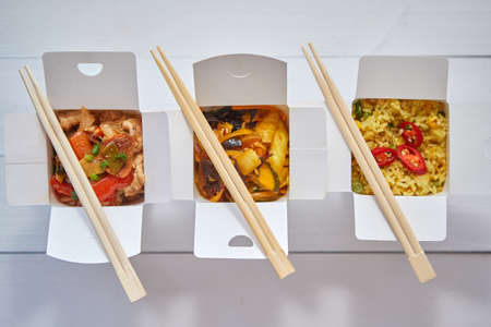 Three take away paper boxes filled with asian food placed in row on white wooden background.の写真素材