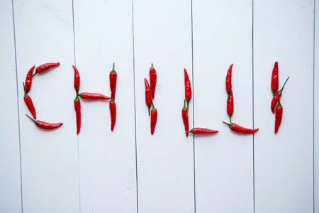 A word CHILLI formed with small red chilli peppers. Placed on white wooden table. Top View.の写真素材