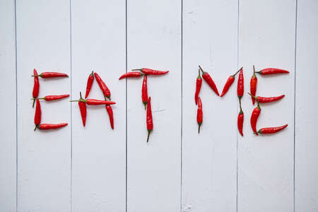 A word EAT ME formed with small red chilli peppers. Placed on white wooden table. Top View.の写真素材