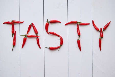 A word TASTY formed with small red chilli peppers. Placed on white wooden table. Top View.の写真素材