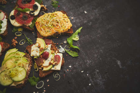 Variety of healthy fresh sandwiches with different vegetables, herbs and ingredients placed on dark table. Close up.の写真素材