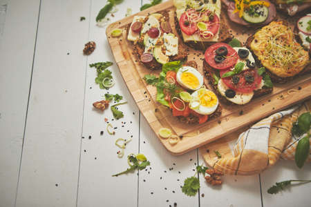 Tasty, homemade small sandwiches with various ingredients served on wooden chopping board. Vege...