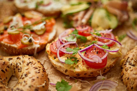 Composition of various homemade bagels sandwiches with sesame and poppy seeds, cream cheese, ham, radish, arugula, cherry tomatoes, cucumbers, hummus, smoked salmon. Close up.の写真素材