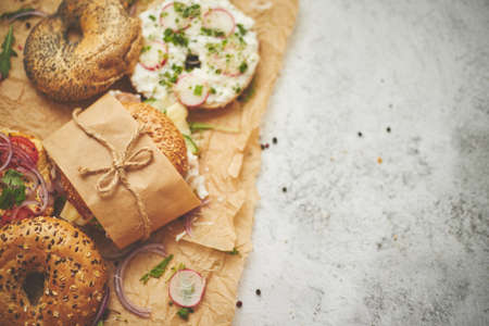 Bagels with Italian ham prosciutto, cream cheese, hummus, radish and salad wrapped in brown baking...