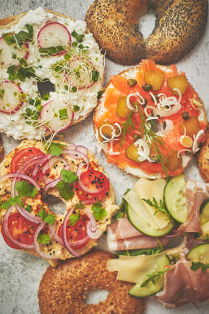 Homemade Bagel sandwiches with different toppings, salmon, cottage cheese, hummus, ham, radish and fresh herbs on a white rusty table, top view. Delicious and healthy breakfast concept.の写真素材