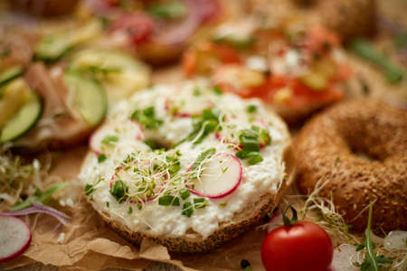 Composition of various homemade bagels sandwiches with sesame and poppy seeds, cream cheese, ham, radish, arugula, cherry tomatoes, cucumbers, hummus, smoked salmon. Close up.の写真素材