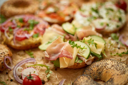 Composition of various homemade bagels sandwiches with sesame and poppy seeds, cream cheese, ham, radish, arugula, cherry tomatoes, cucumbers, hummus, smoked salmon. Close up.の写真素材