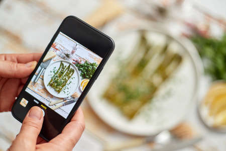 Woman taking picture of fresh prepared food with smartphone for social media. Roasted aparagus with herbs and parmesan.の写真素材