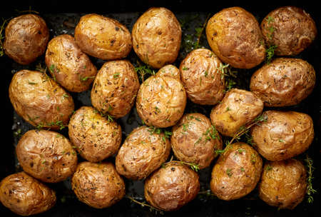 Oven baked whole potatoes with seasoning and herbs in metalic tray. Roasted potatoes in jackets. Top view. Close up.の写真素材