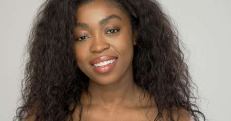 Attractive black female model with curly hair smiling and looking at camera against gray backgroundの写真素材