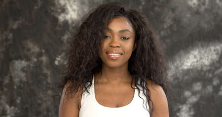 Happy African American female in white top smiling and looking at camera against rough gray wallの写真素材