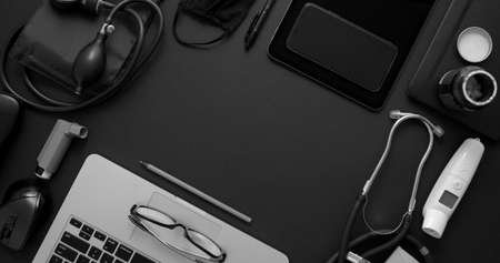Doctor desktop concept. Various medical tools and accessories placed on black background table as a mockup. With laptop, medicine, stethoscope, pressure gauge, thermometer. Flat lay, top view with copy space.の写真素材