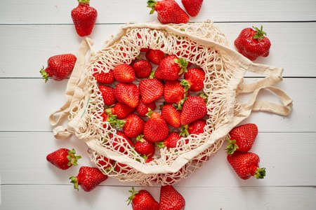 Fresh strawberries in eco-friendly package on white wooden background. Vegetarian healthy organic meal from the market. Zero waste conceptの写真素材