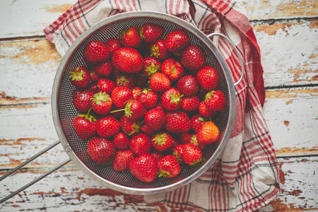 Freshly harvested strawberries. Metal colander filled with juicy fresh ripe red strawberries on an old wooden textured table. Top view.の写真素材