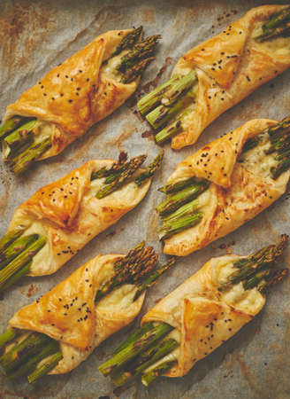 Baked green asparagus in puff pastry sprinkled with sesame seeds and cheese. Placed on a white baking paper background. Close-up, top view, flat lay.の写真素材