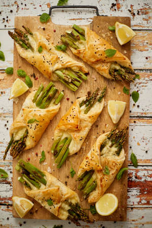 Grilled green asparagus and cheese puff pastry folded as envelope and topped with black sesame seeds placed on wooden cutting board. Top view, flat lay.の写真素材