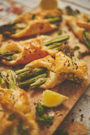Baked green asparagus wrapped in puff pastry. Served on wooden board. Top view, flat lay. Selective focusの写真素材