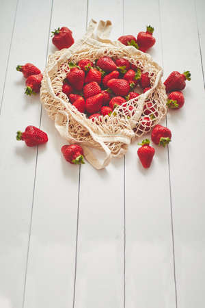 Fresh strawberries in eco-friendly package on white wooden background. Vegetarian healthy organic meal from the market. Zero waste conceptの写真素材