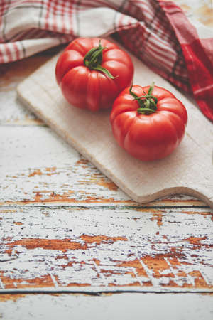 Top view of a white cutting board with a fresh juicy tomatoes on a wooden rustical table.の写真素材