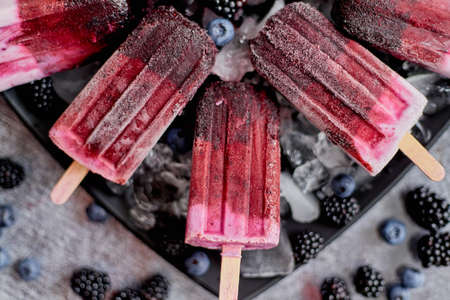 Homemade fresh frozen blueberry and blackberry ice cream on black plate with ice sitting on stone table with fresh berries on side. Top view, flat layの写真素材
