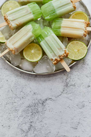 Delicious lime and cream homemade ice creams placed with ice cubes on gray stone backdrop. Flat lay, top view with copy spaceの写真素材