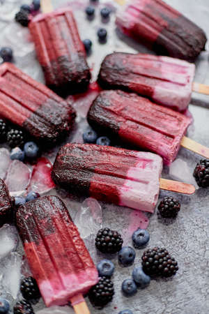 Homemade blackberry and cream ice-creams with frozen berries on black slate tray over dark grunge backdrop. Top view, flat lay.の写真素材