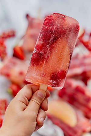 Close up on kids hand holding colorful red berry fruit ice cream. Healthy summer snack concept. Selective focus.の写真素材