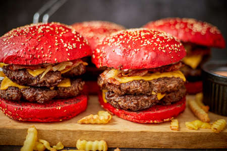 Bunch of tasty burgers with red buns and fresh french fries placed on wooden boardの写真素材