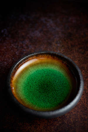 Handmade brown and green glaze rustic pottery bowl placed on rusty backgroundの写真素材