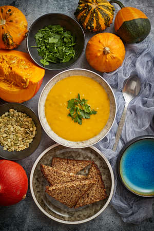 Pumpkin soup decorated with parsley for Thanksgiving, halloween. Placed on grey stone background. Top view, flat lay. Composition of autumn vegetables with mini pumpkins.の写真素材