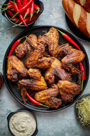 Grilled chicken wings with chilli pepper on a rustic plate served with various dips and breadの写真素材